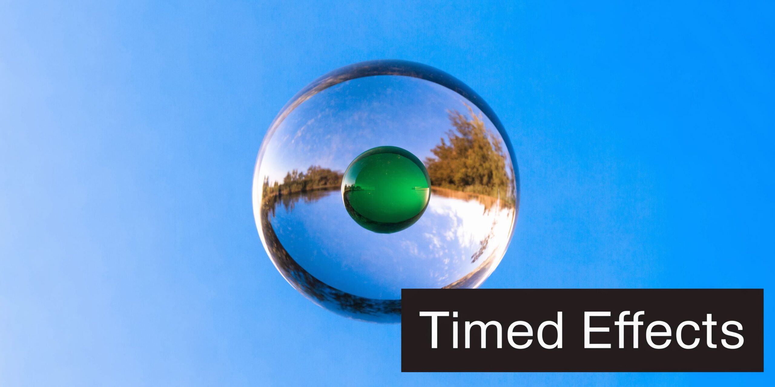 A large clear glass sphere containing a smaller green sphere floating against a bright blue sky background.