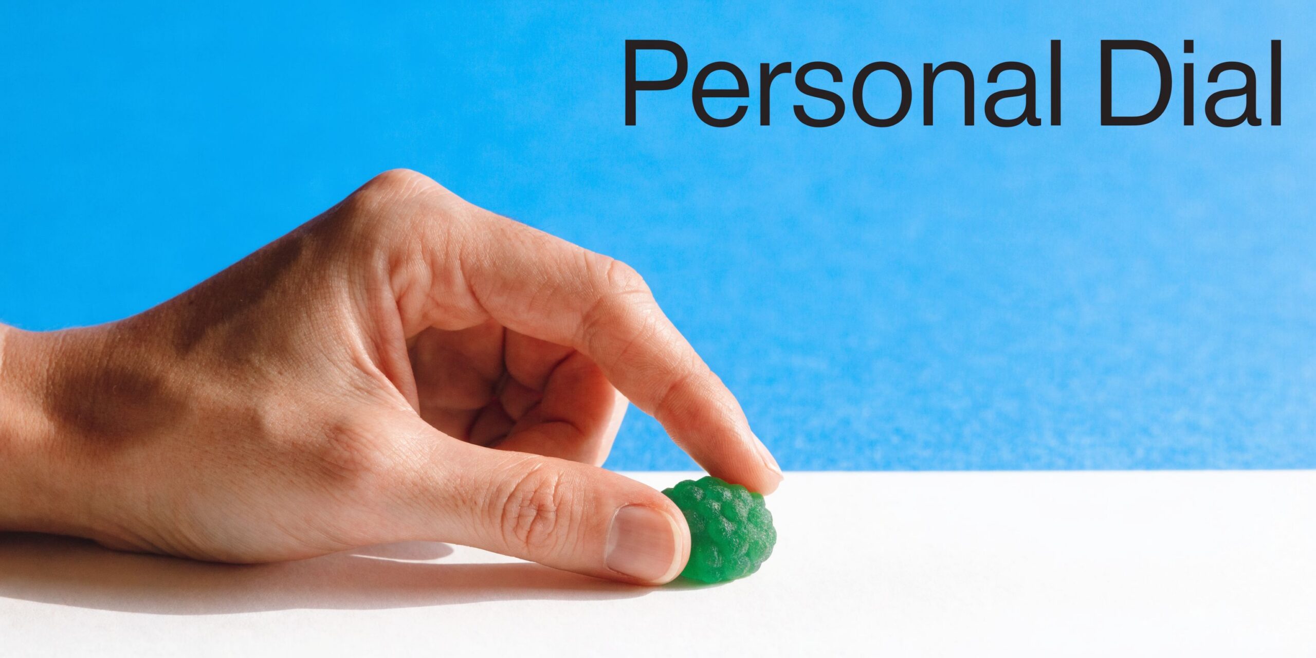 A hand placing a green candy on a white surface against a bright blue background