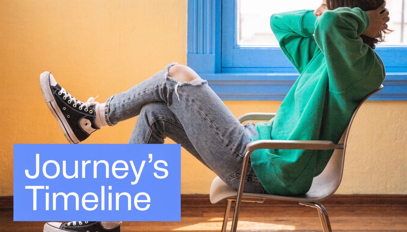 A relaxed person wearing a green sweatshirt and ripped blue jeans sitting on a metal chair.