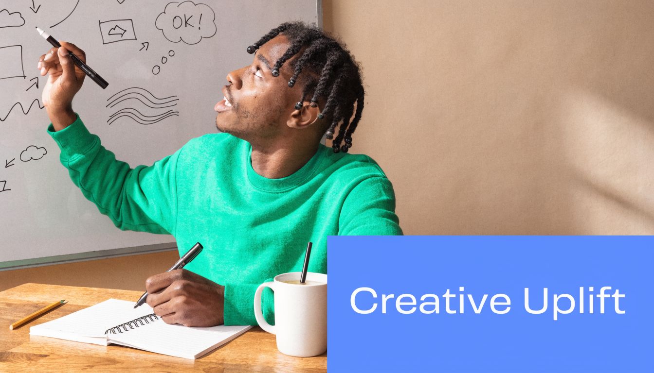 A young creative person in a green sweater brainstorming and drawing on a whiteboard at a desk.